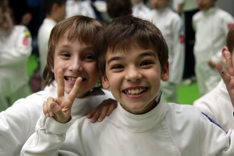 Young fencers in gear smiling together at a fencing tournament